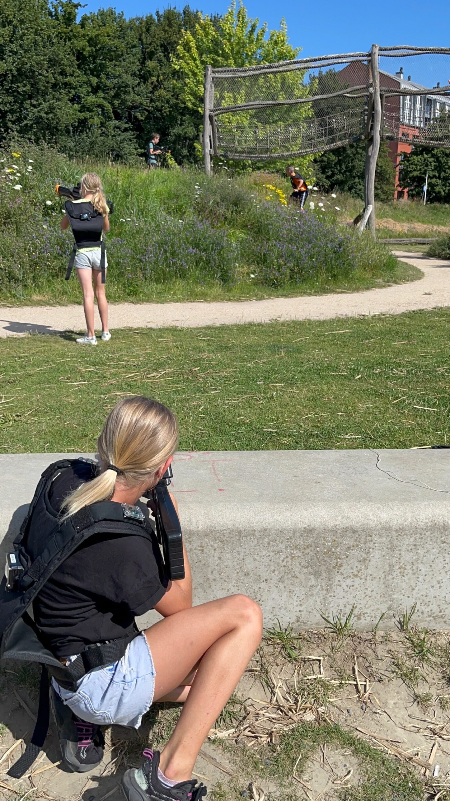 Een stoere actiefoto van een kind dat door een scope kijkt, buiten in een park/bos.